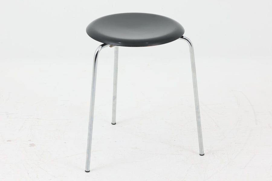 1954年、デンマークのデザイナー、Arne Jacobsen（アルネ・ヤコブセン）によって発表された3本脚のスツール、「DOT（ドット）」。このスツールは、ヤコブセンが手がけた「ルードブレ市庁舎」のロビーで待合席として使用されていました。3本脚のモデルはビンテージ品のみで入手可能です。オフィスや自宅での日常的な使用はもちろん、予備の椅子としても便利なこのスツールは、シンプルなデザインが魅力です。座面の中央がわずかにくぼんでおり、座った際にフィット感を生み出します。シンプルながらもヤコブセンのこだわりが感じられ、また、単なるスツールとしてだけでなく、ソファの横に置いて本や小物を置くサイドテーブルとしても活用できます。