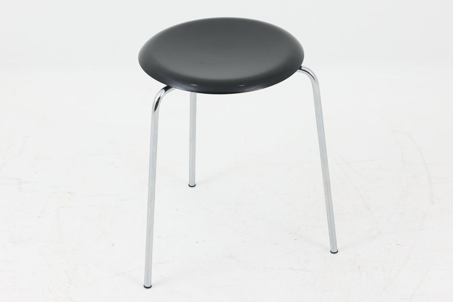 1954年、デンマークのデザイナー、Arne Jacobsen（アルネ・ヤコブセン）によって発表された3本脚のスツール、「DOT（ドット）」。このスツールは、ヤコブセンが手がけた「ルードブレ市庁舎」のロビーで待合席として使用されていました。3本脚のモデルはビンテージ品のみで入手可能です。オフィスや自宅での日常的な使用はもちろん、予備の椅子としても便利なこのスツールは、シンプルなデザインが魅力です。座面の中央がわずかにくぼんでおり、座った際にフィット感を生み出します。シンプルながらもヤコブセンのこだわりが感じられ、また、単なるスツールとしてだけでなく、ソファの横に置いて本や小物を置くサイドテーブルとしても活用できます。